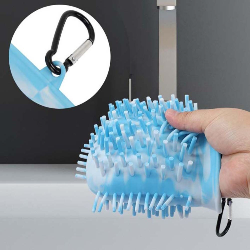 Blue and white grooming brush with a carabiner handle held by a hand against a gray background.